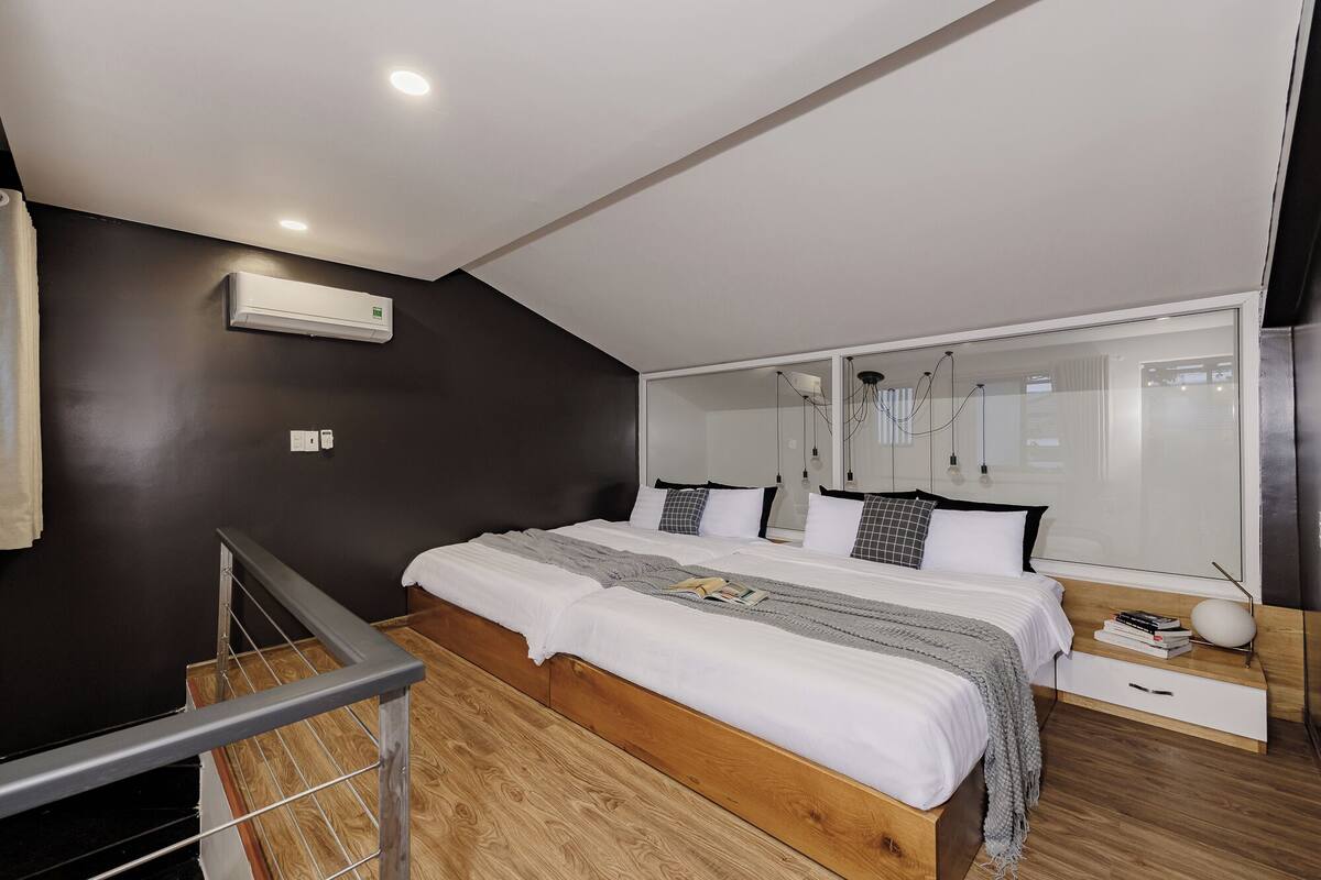 A modern bedroom with a large bed, a wooden floor, a black wall, and a ceiling with recessed lighting.