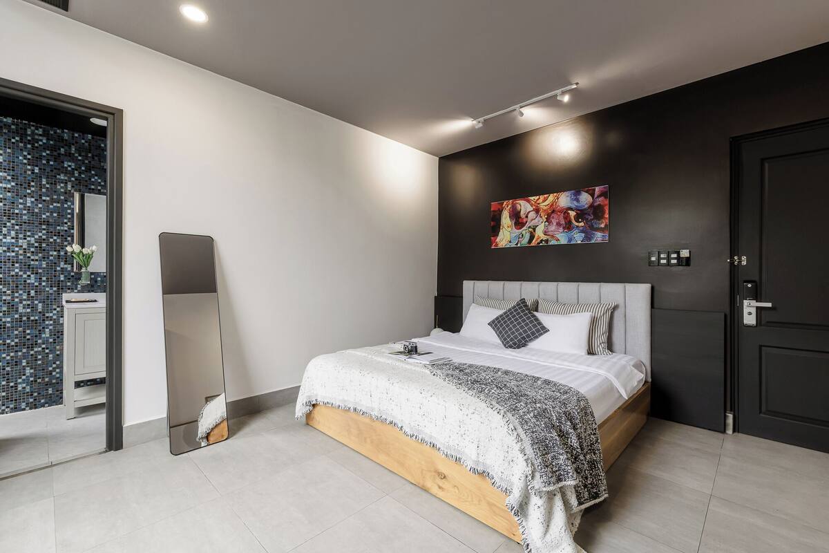 A modern bedroom with a bed, a large mirror, a colorful abstract painting, and a door.