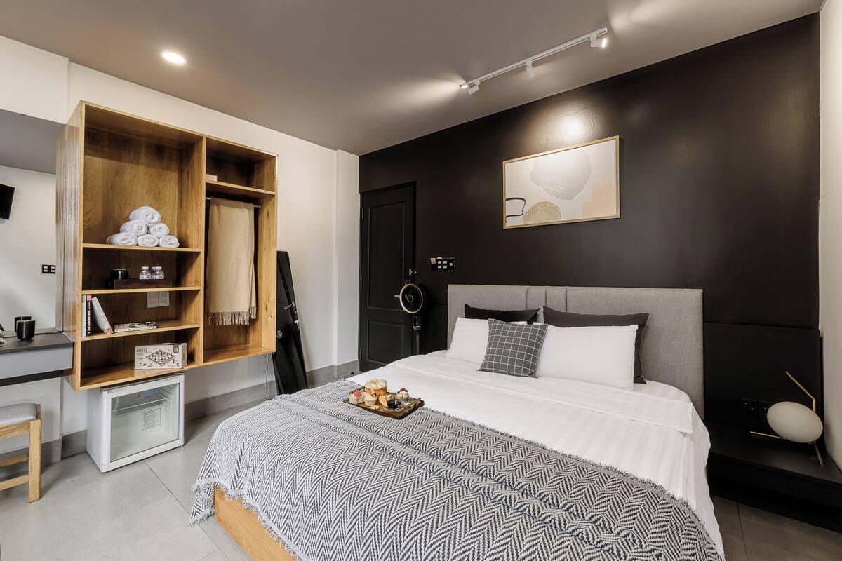 A modern bedroom with a bed, a wardrobe, a desk, and a wall-mounted artwork.