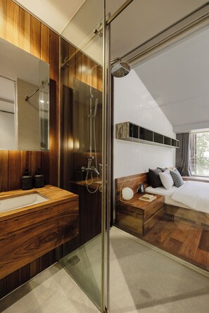 A modern bedroom with a wooden vanity, a glass shower enclosure, a bed with a view, and a mounted shelf. - The K'rin Villa (Da Lat)