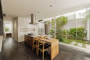 A modern kitchen with a central island, wooden chairs, and a large window overlooking a garden. - The K'rin Villa (Da Lat)