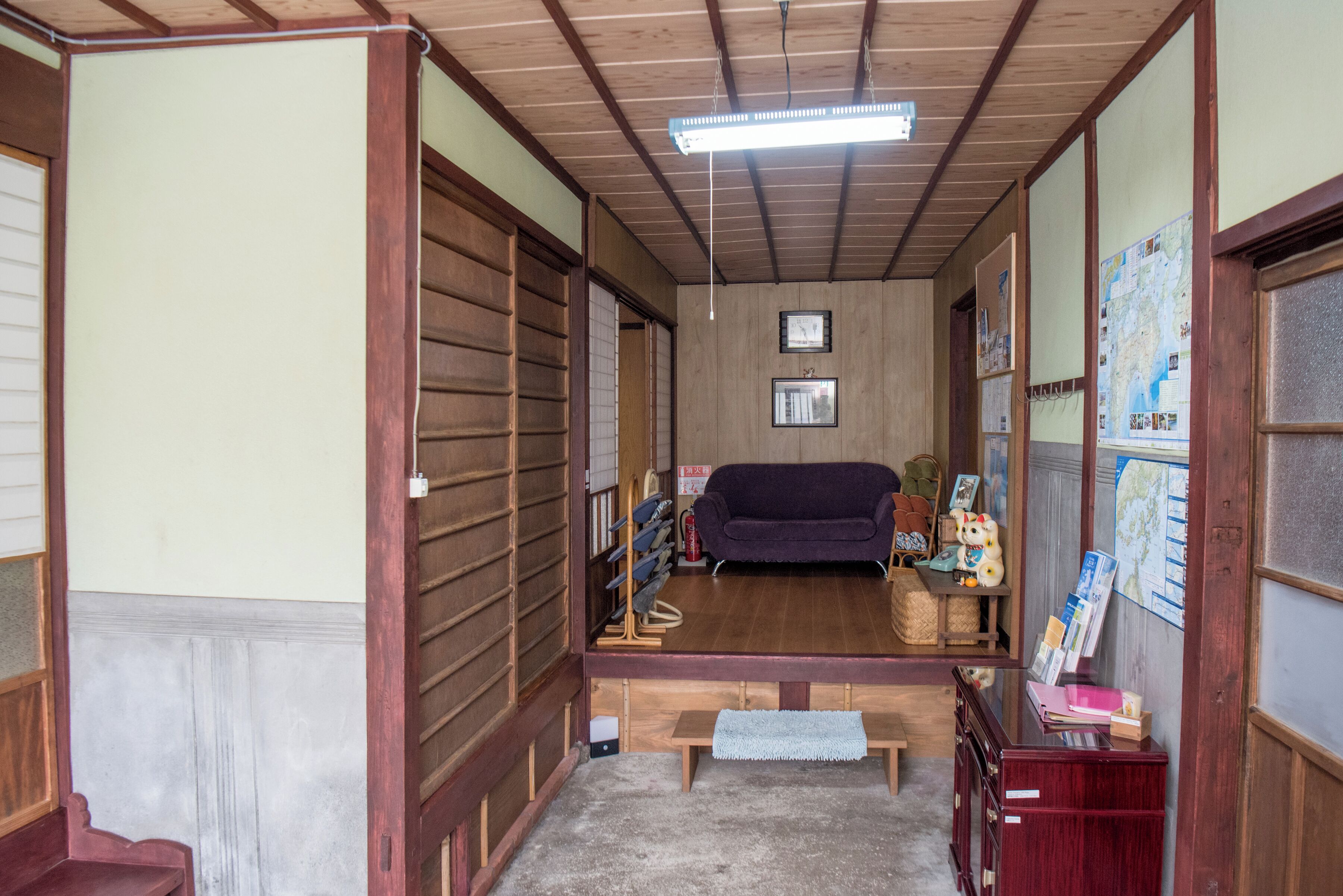 A traditional Japanese room with tatami flooring, a low wooden bench, a purple sofa, and a wooden cabinet with various items.