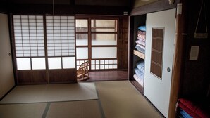 Ein traditioneller japanischer Raum mit Tatami-Böden, verschiebbaren Shoji-Türen, einem Holzsessel und einem Bett mit Futon-Auflage.