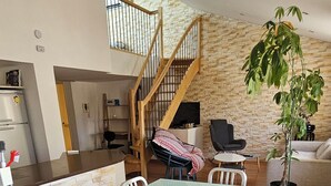 A spacious dining area with a glass-top table and modern chairs, a staircase with wooden railings, and a living area with a sofa and a potted plant. - 3* family duplex near the sea, Spain and the mountains. Pets allowed (Le Boulou)