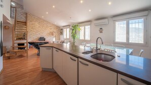 A modern kitchen with a wooden staircase, white cabinets, and a large island with a sink. - 3* family duplex near the sea, Spain and the mountains. Pets allowed (Le Boulou)