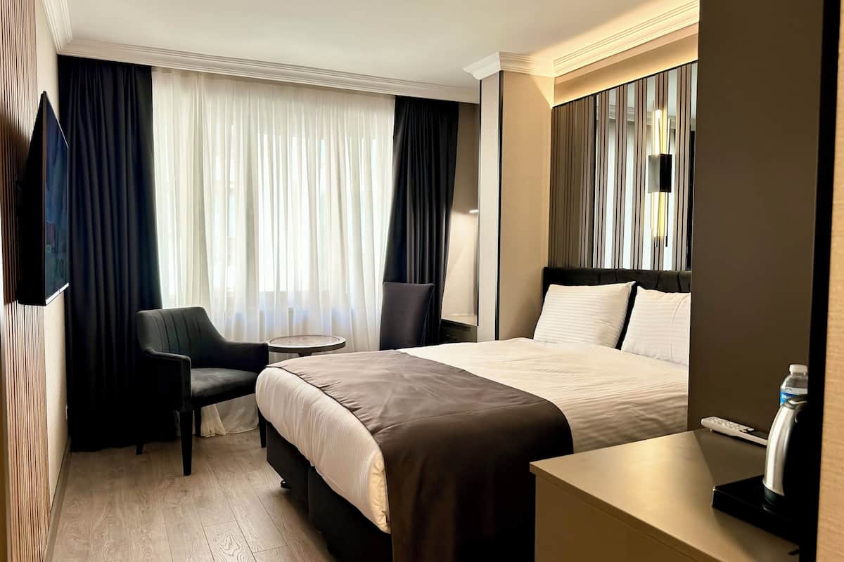 A hotel room with a bed, a desk, a chair, a small table, and a TV.