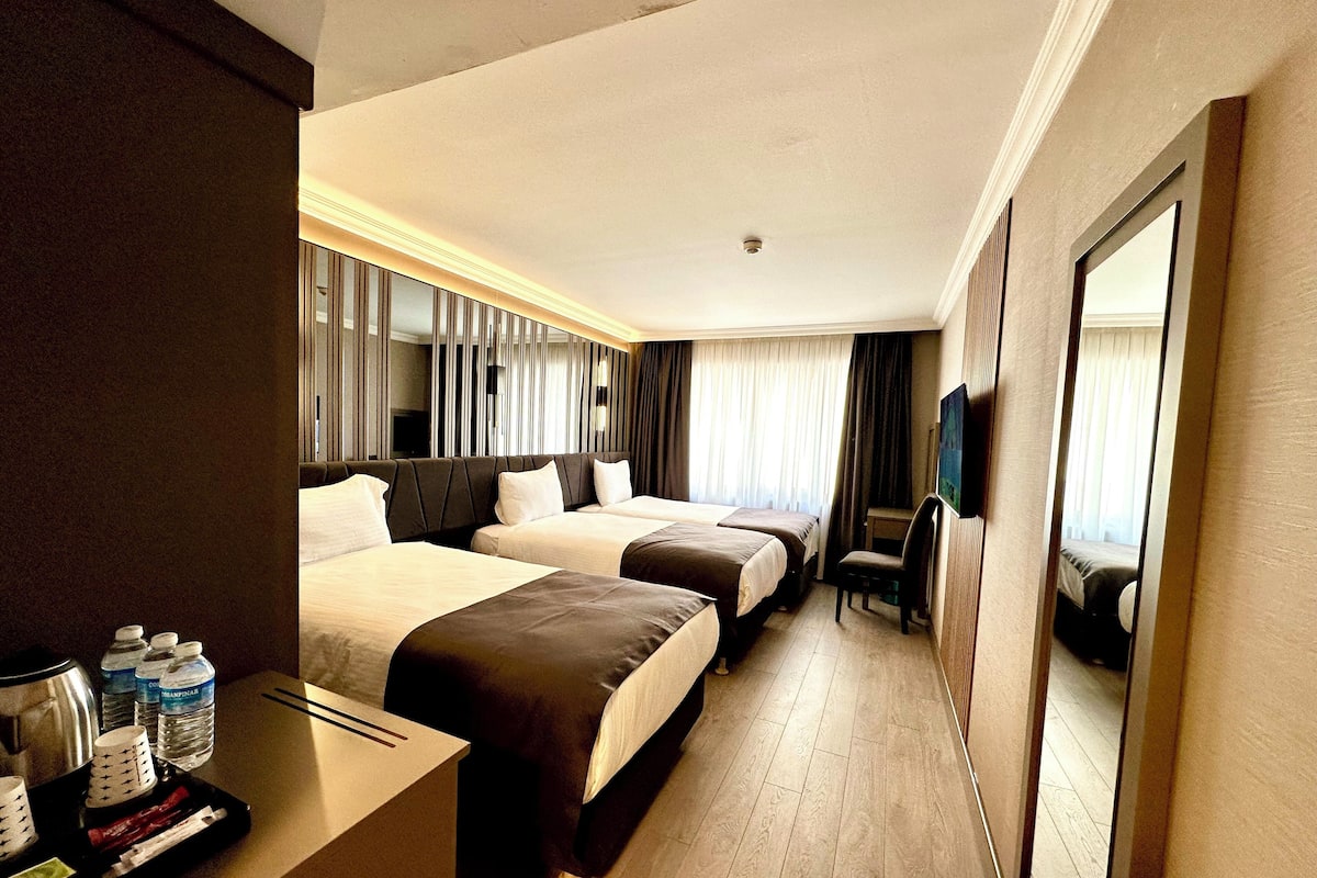 A hotel room with two beds, a desk with a tray of toiletries, a chair, and a television.