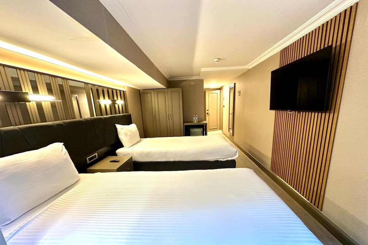 A hotel room with two beds, a television, a small table with a remote, and a wall-mounted TV.