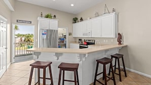 Cocina con isla central, armarios blancos y vista al exterior, identificada como "Beach Bungalow".