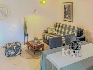 Un salon avec un canapé à carreaux, une table basse, une horloge, une lampe et un tableau encadré accroché au mur.