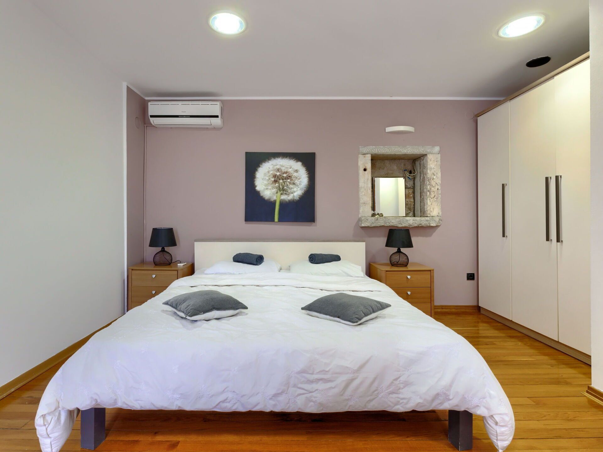 Ein Schlafzimmer mit Bett, Nachttischen, einem Spiegel und einem Wandbild mit einem Löwenzahn.