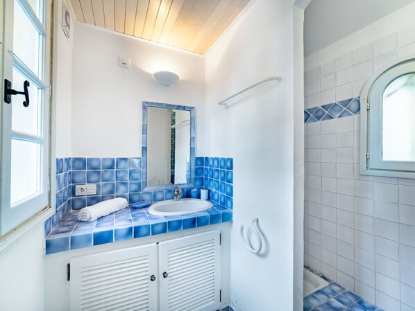 A bathroom with a white sink, blue-tiled backsplash, and a mirror.