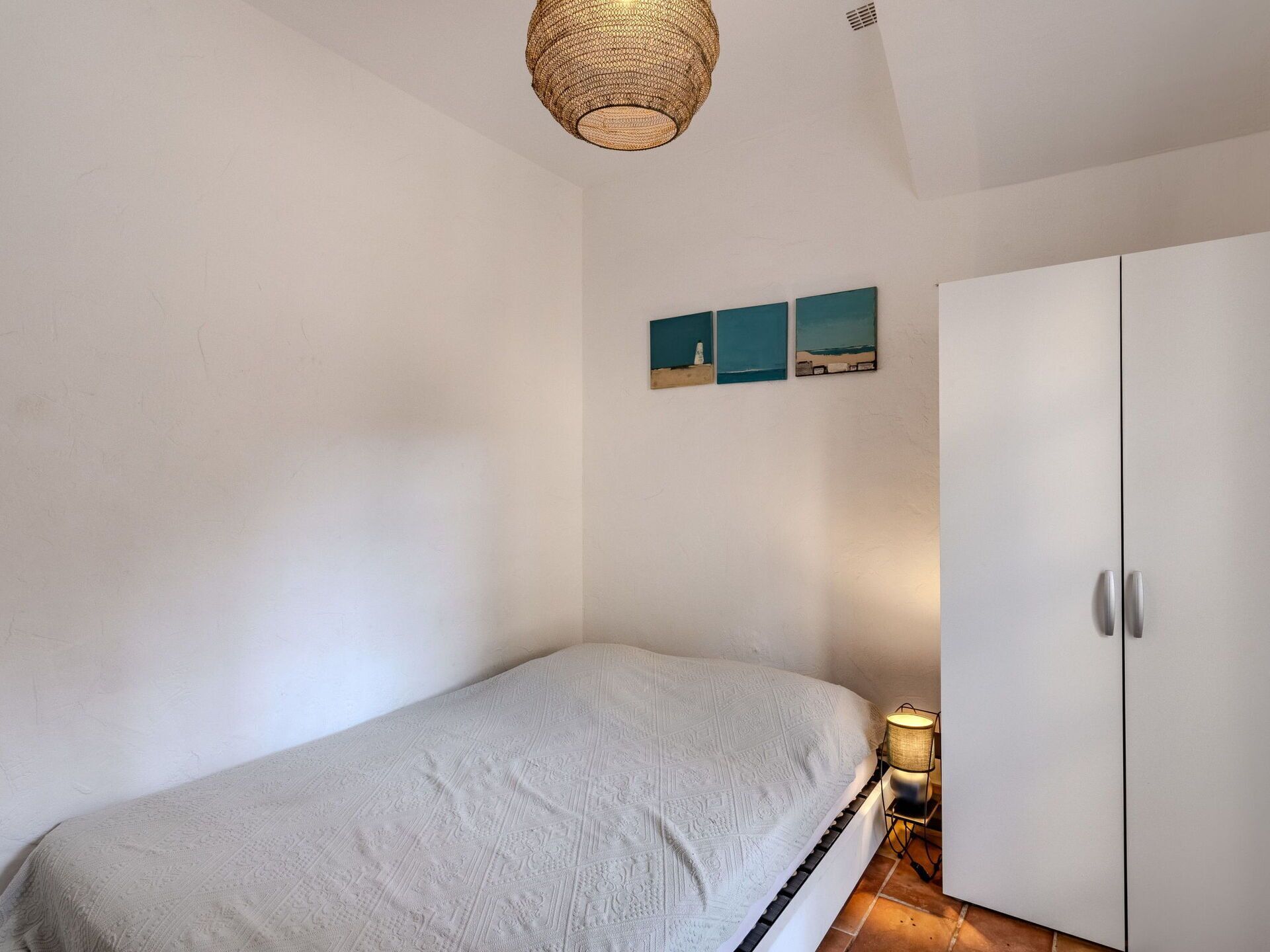 A bedroom with a bed, a wardrobe, and a wall-mounted shelf with three framed pictures.