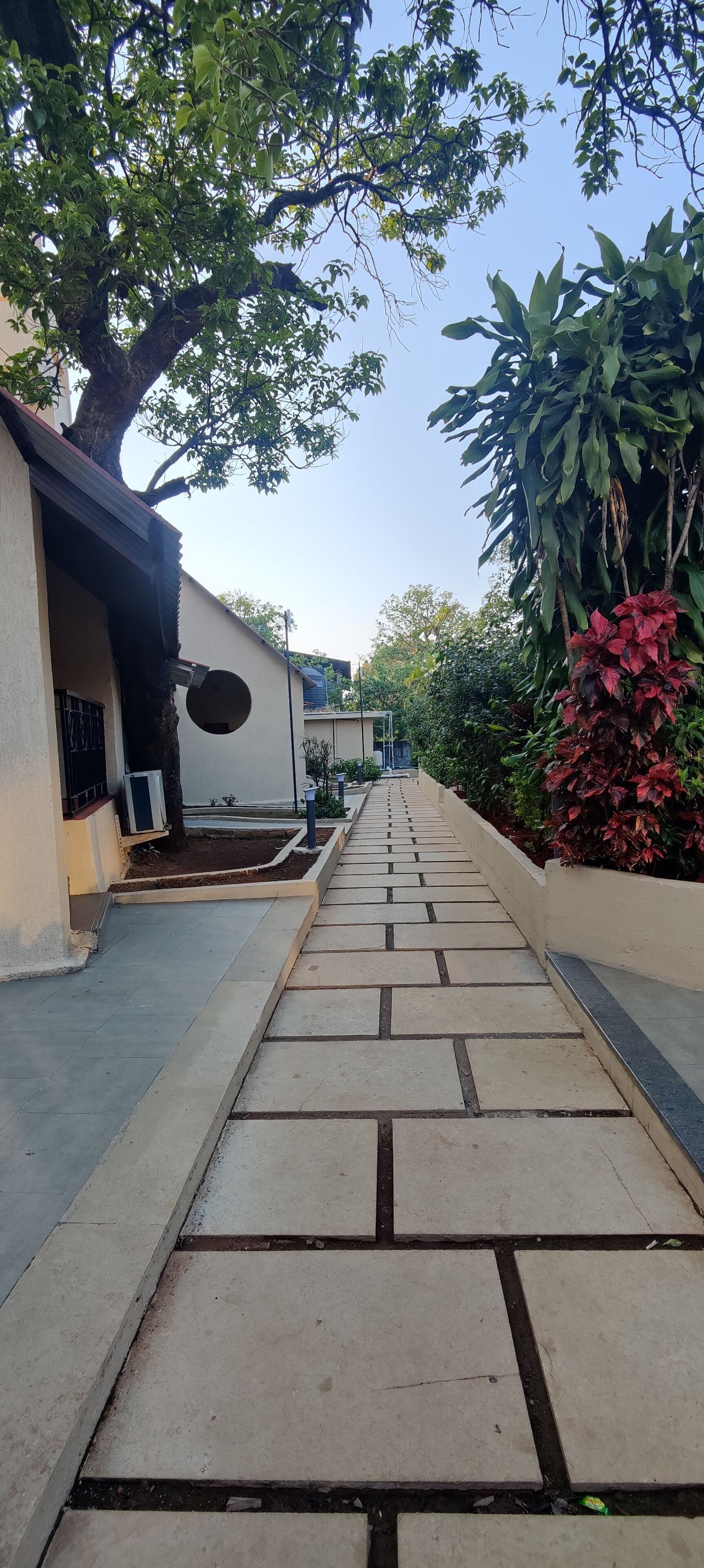 A pathway leading to a building with a covered entrance, surrounded by greenery and a clear sky.