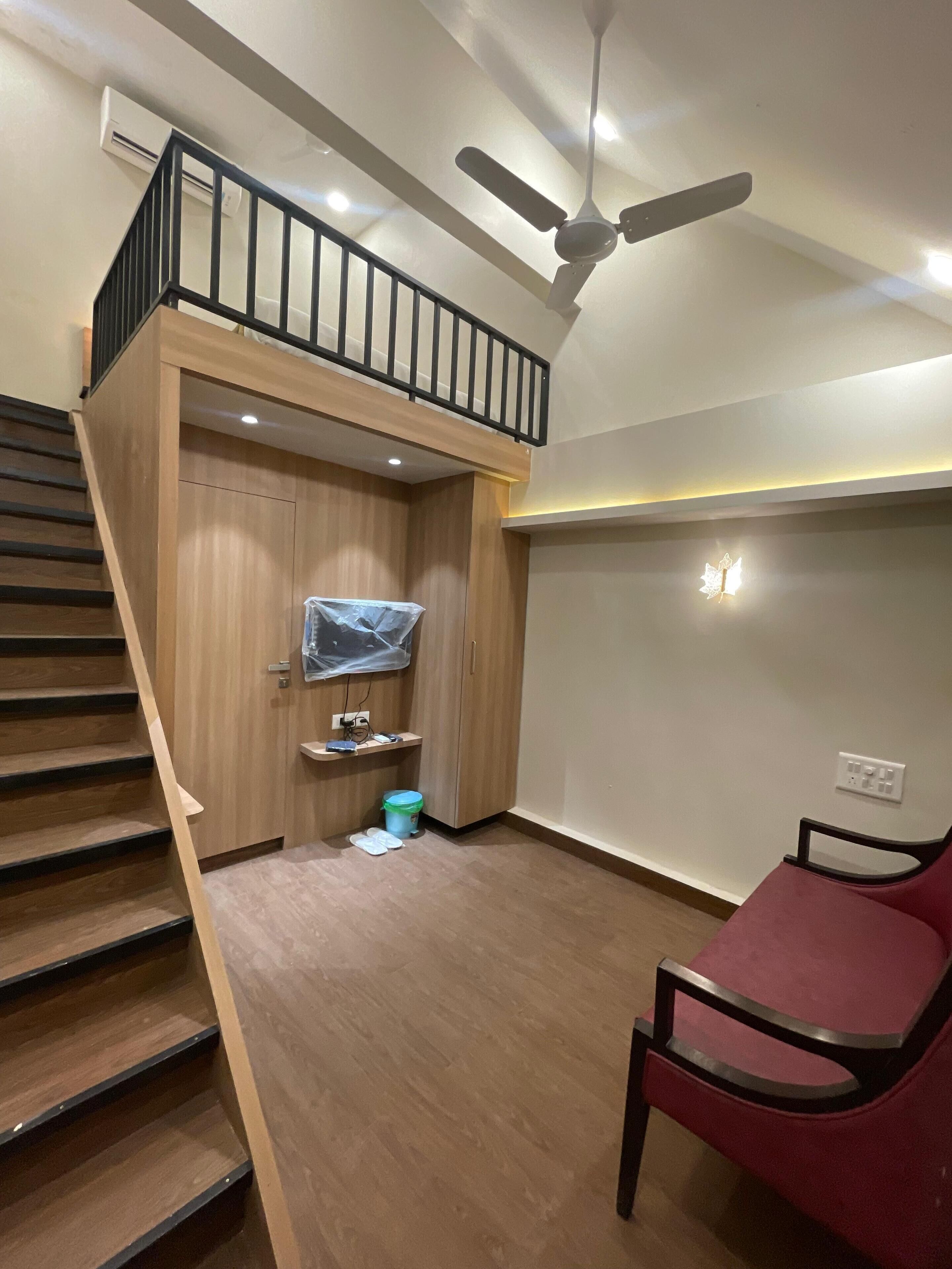 A room with a wooden staircase, a ceiling fan, a red chair, and a small table with a plastic container.