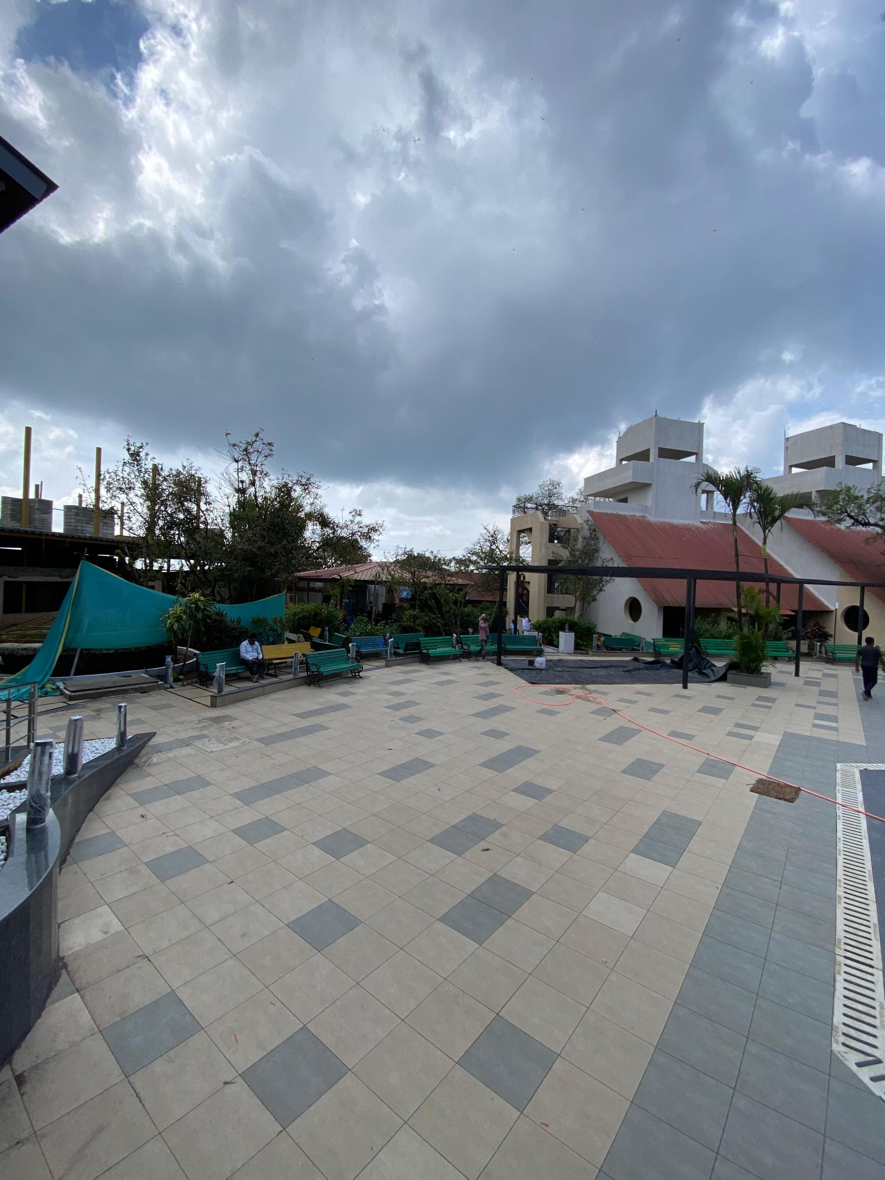 A spacious outdoor area with a tiled floor, green benches, and a few people.