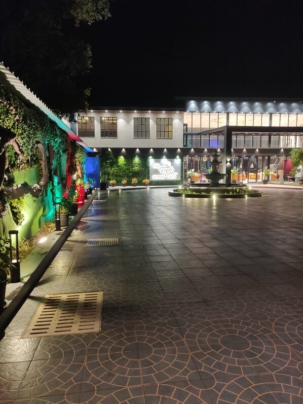 A hotel entrance with a modern design, featuring a well-lit pathway, a fountain, and a variety of plants and greenery. - The Byke Shanti Villa  (Mahabaleshwar)