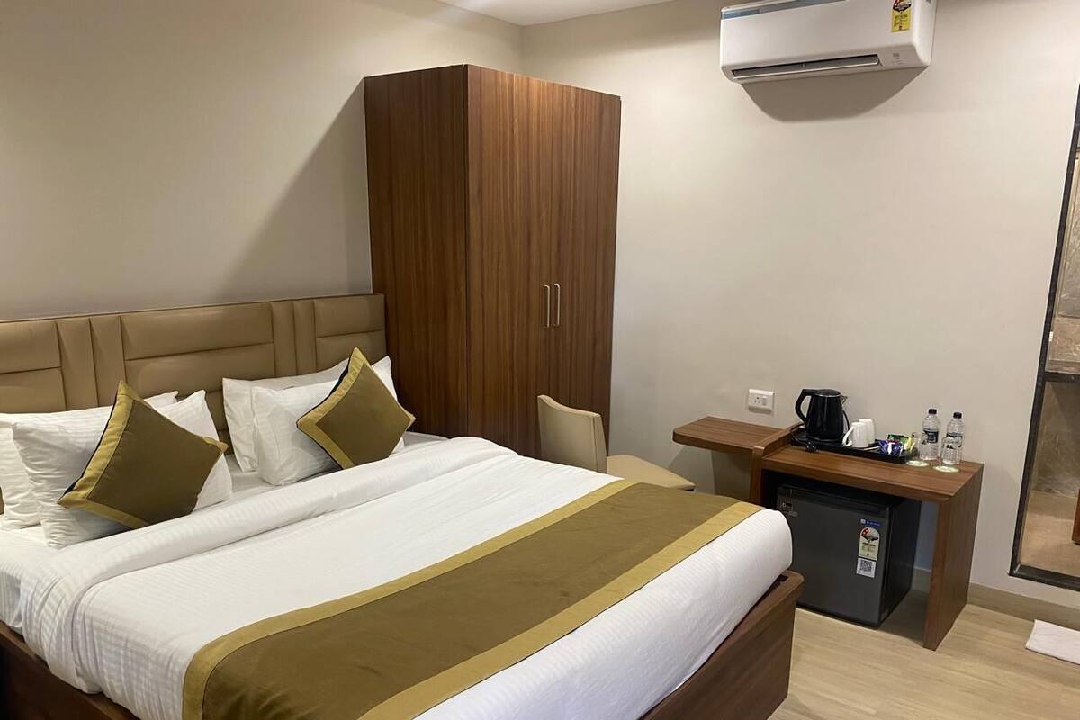 Een hotelkamer met een groot bed, een houten garderobe, een klein bureau met een koffiezetapparaat en een airconditioning.