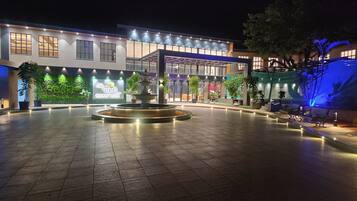 A well-lit courtyard with a central fountain, surrounded by potted plants and a modern building facade.