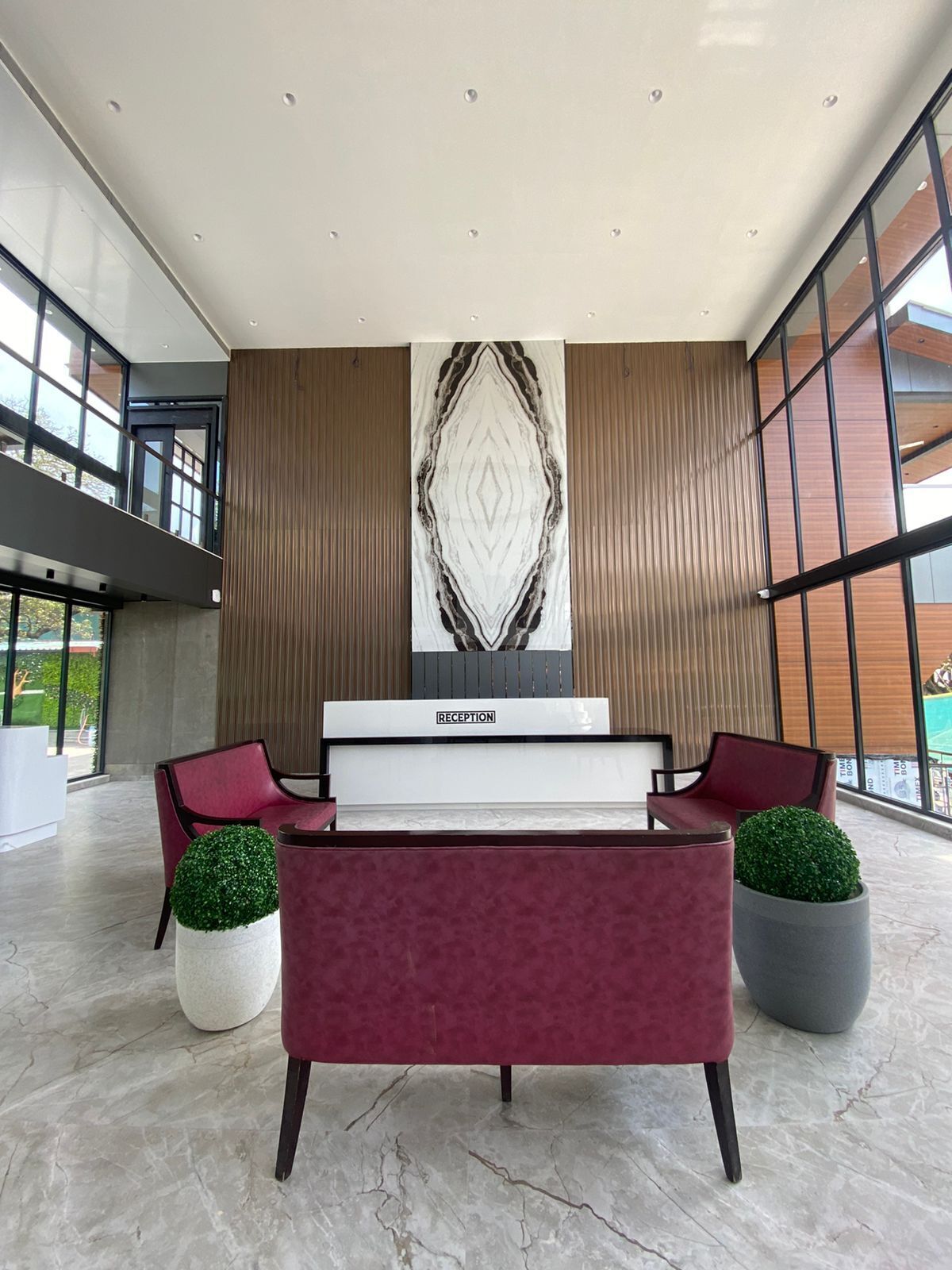 A reception area with a reception desk, two red cushioned chairs, and two potted plants.