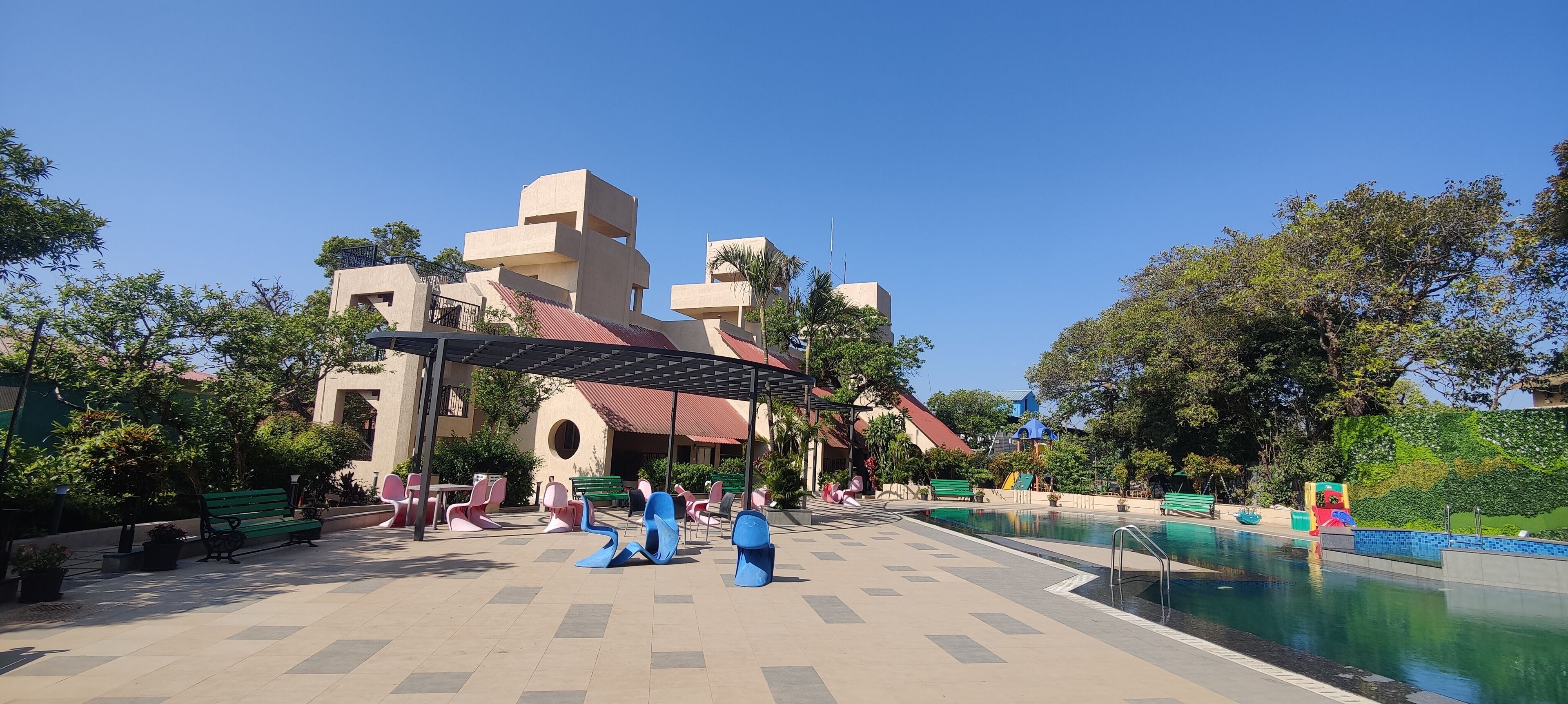 A pool area with a modern building, benches, and a covered seating area.