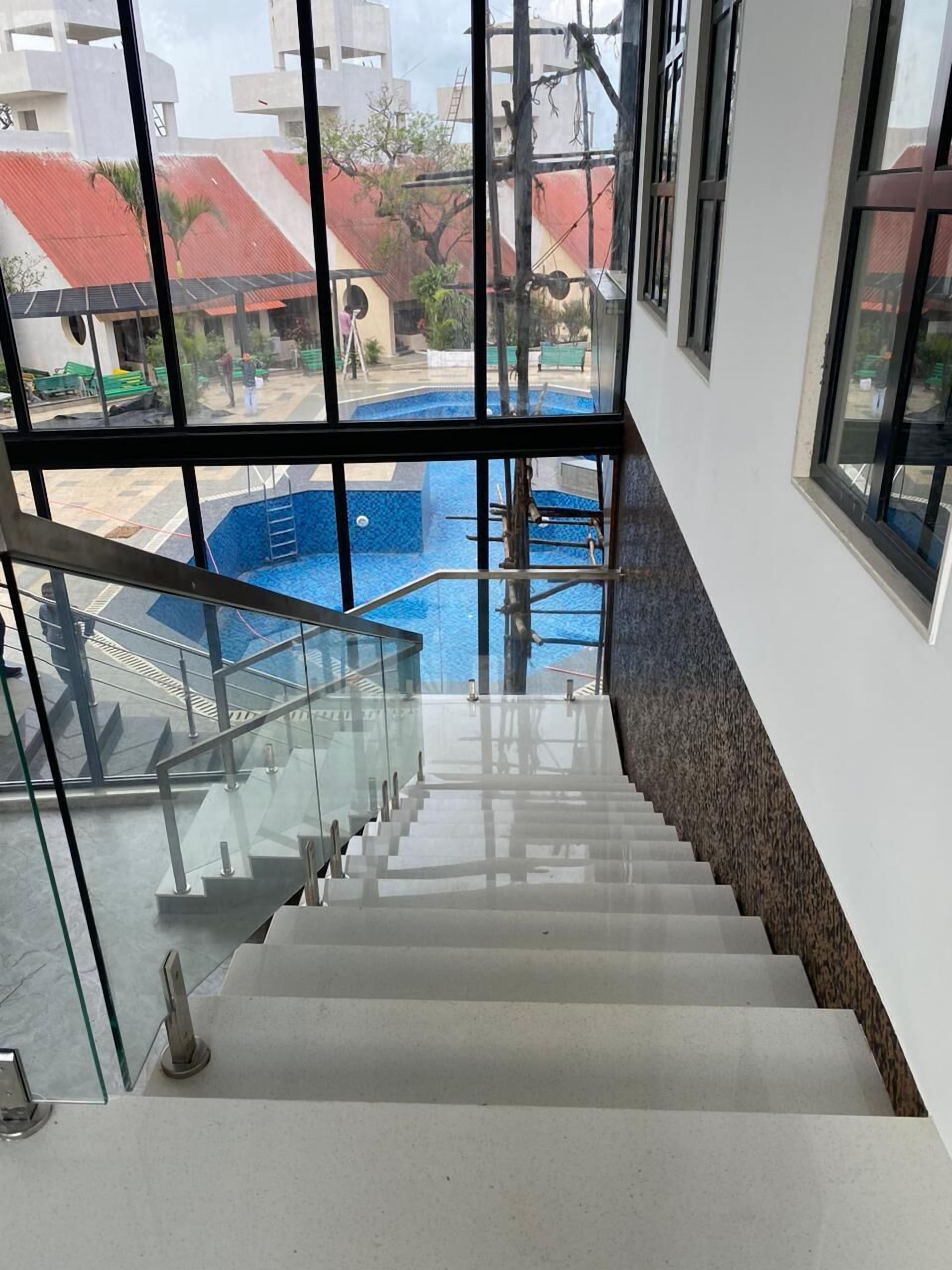 Una escalera conduce a una zona de piscina con vistas a edificios y una estructura de techo rojo al fondo.