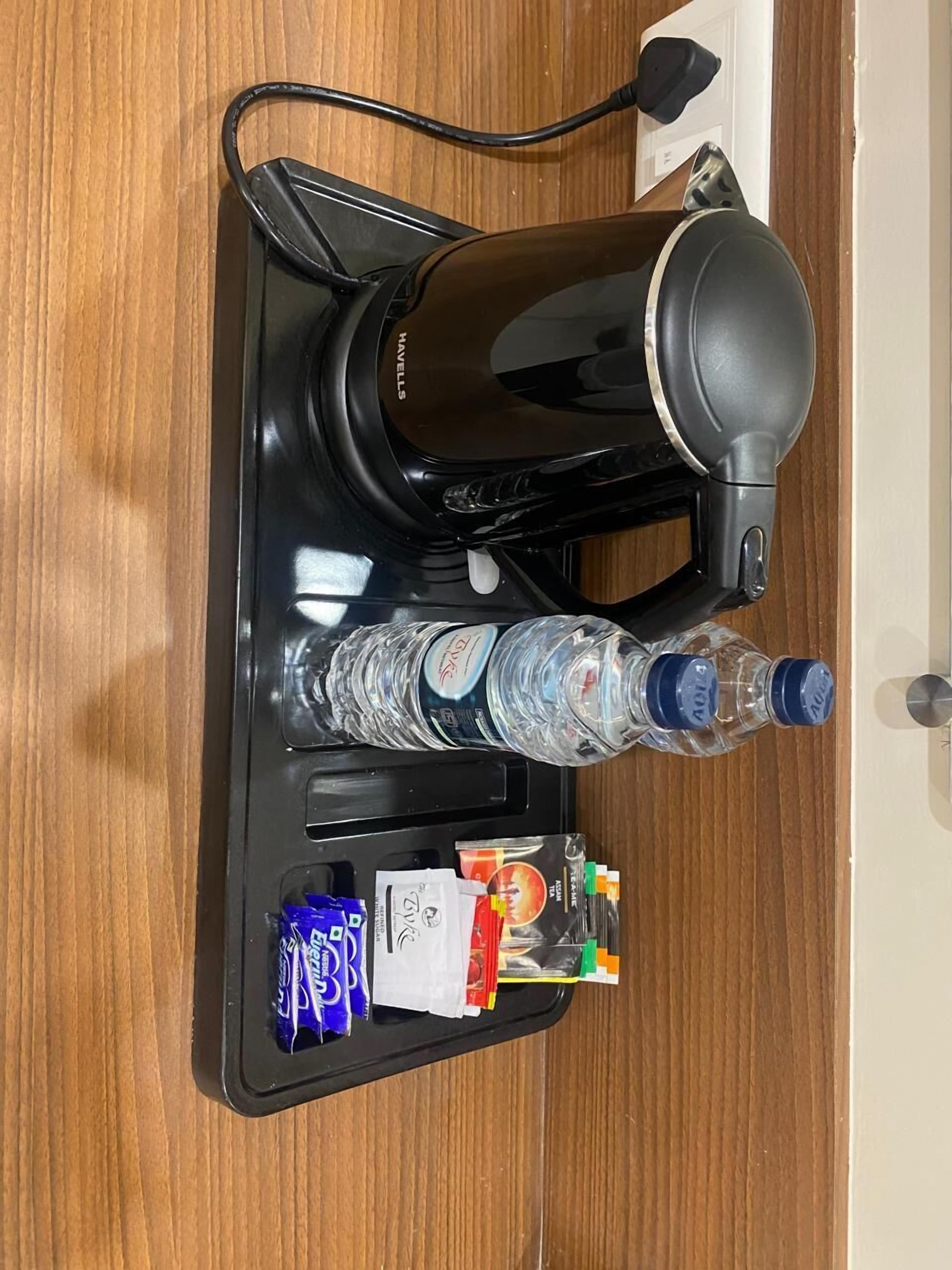 Eine Kaffeemaschine mit Kabel, zwei Wasserflaschen und ein Tablett mit Snacks und einer Karte.