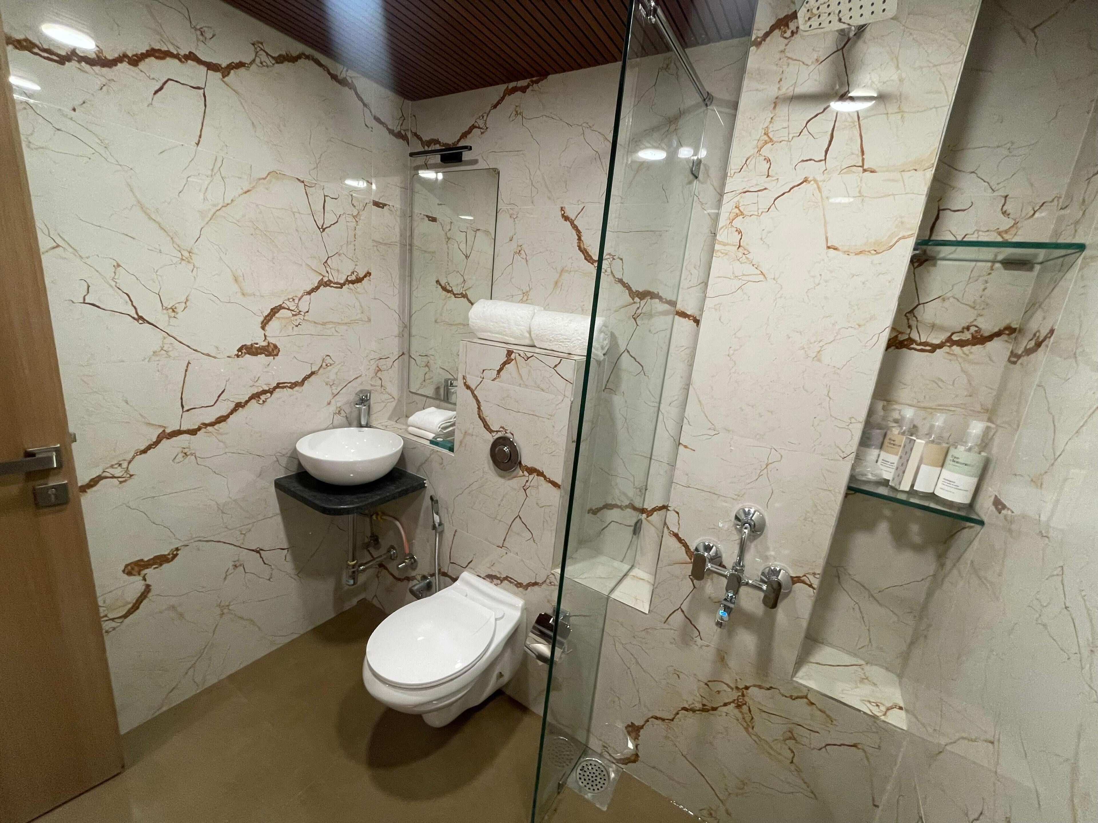 Un baño moderno con salpicadero de mármol, ducha con cerramiento de vidrio, inodoro y lavamanos con encimera negra.