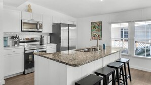 A modern kitchen with white cabinetry, stainless steel appliances, a granite countertop, and a small island with bar stools.