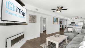 A modern living room with a fireplace, a ceiling fan, and a dining area with a light-colored table and gray sofa.