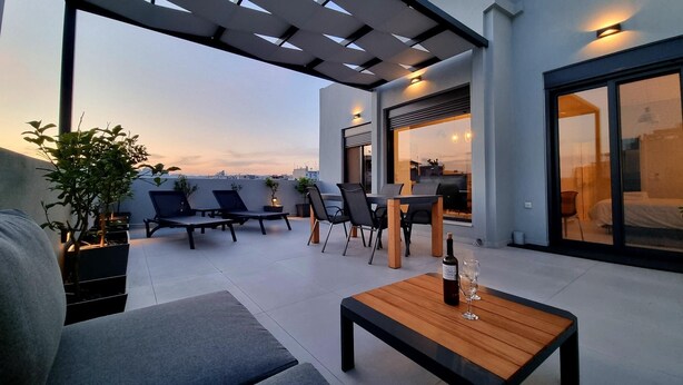 A rooftop terrace with a sofa, lounge chairs, a wooden table with a bottle and glass, and a pergola. - 10 Apartments & Suites Athens (Kallithea)