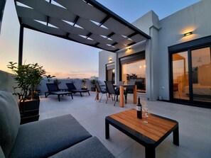 Une terrasse sur le toit avec un canapé, des fauteuils de jardin, une table en bois avec une bouteille et un verre, et une pergola.