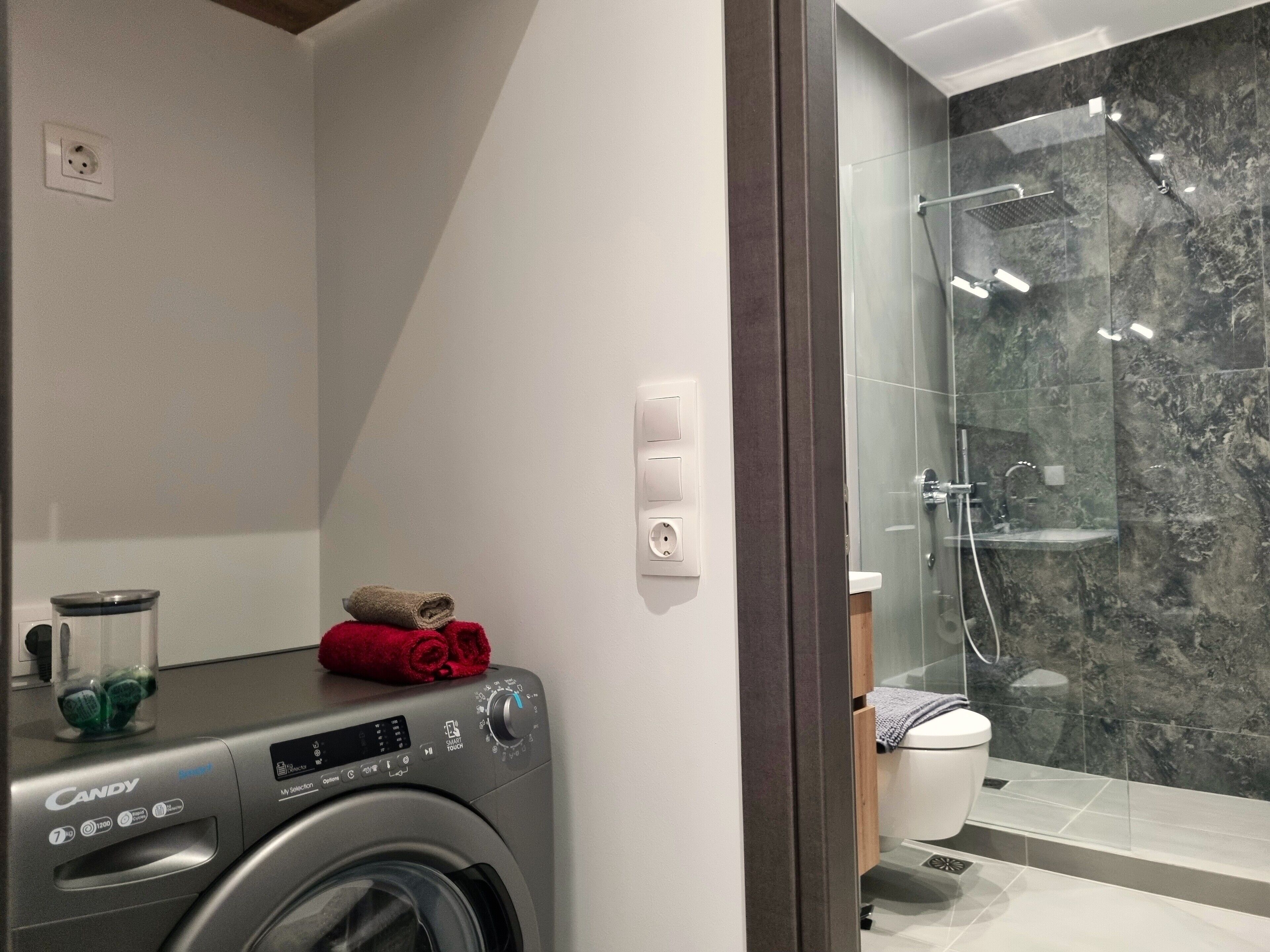 A modern bathroom with a washing machine, a glass shower enclosure, and a toilet.