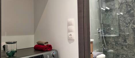 A modern bathroom with a washing machine, a glass shower enclosure, and a toilet.