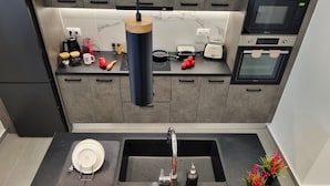 A modern kitchen with a built-in oven, microwave, and toaster. There is a sink with a faucet, a cutting board with vegetables, and a knife. - 10 Apartments & Suites Athens (Kallithea)