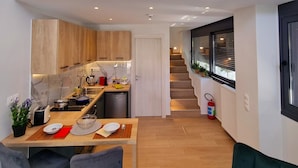 A modern kitchen with a dining area, a staircase leading to an upper level, and a view of the outside through large windows. - 10 Apartments & Suites Athens (Kallithea)