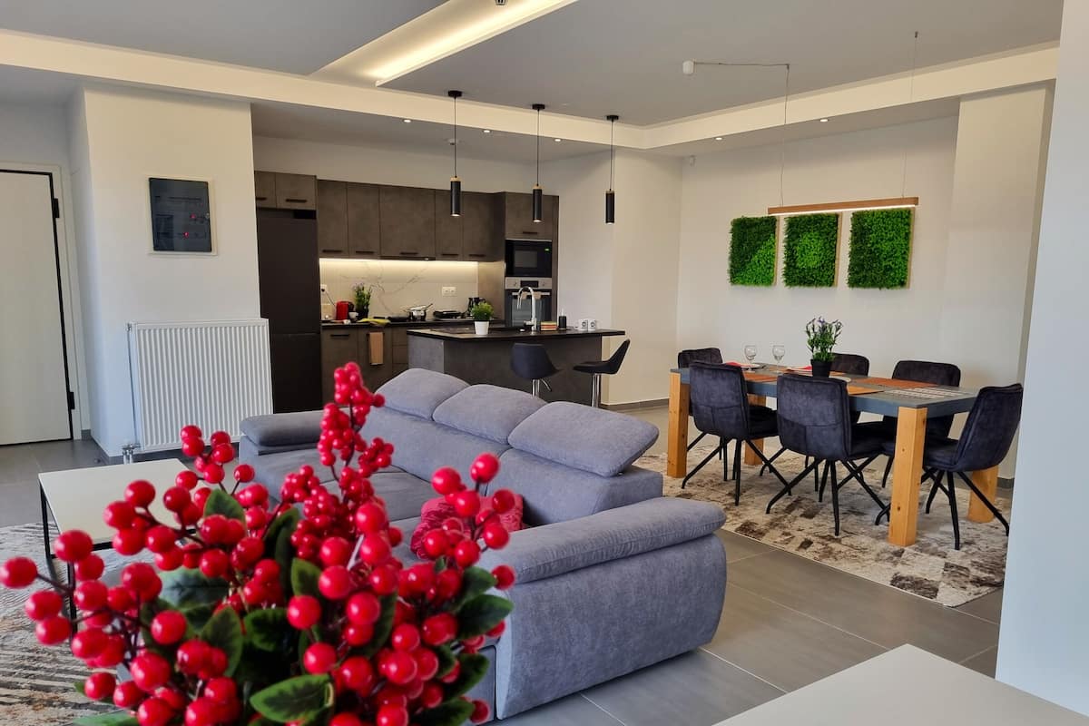 A modern living room with a grey sofa, a dining area with a wooden table and chairs, and a kitchen in the background.