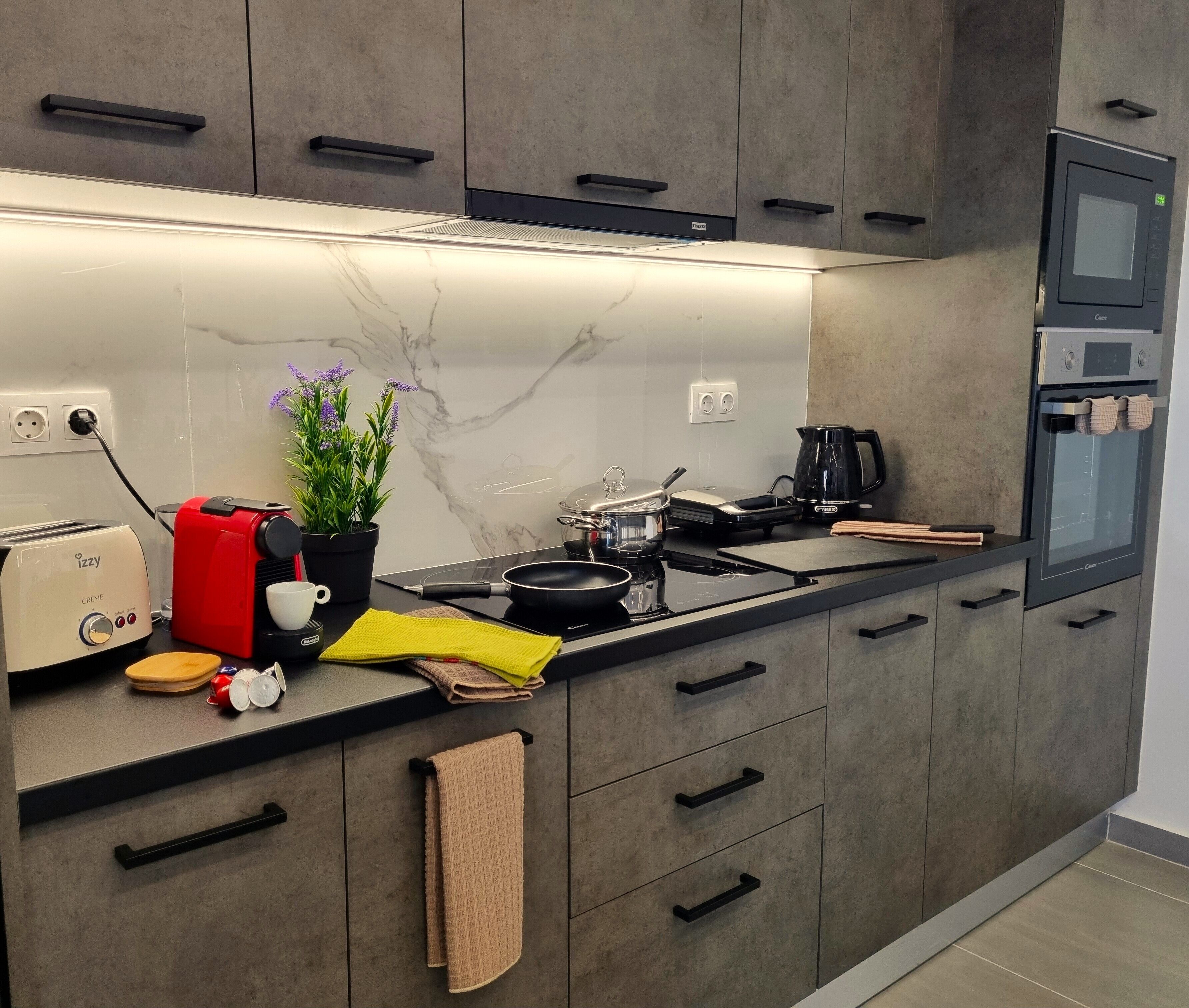 A modern kitchen with grey cabinets, a built-in oven, a coffee maker, and a toaster.