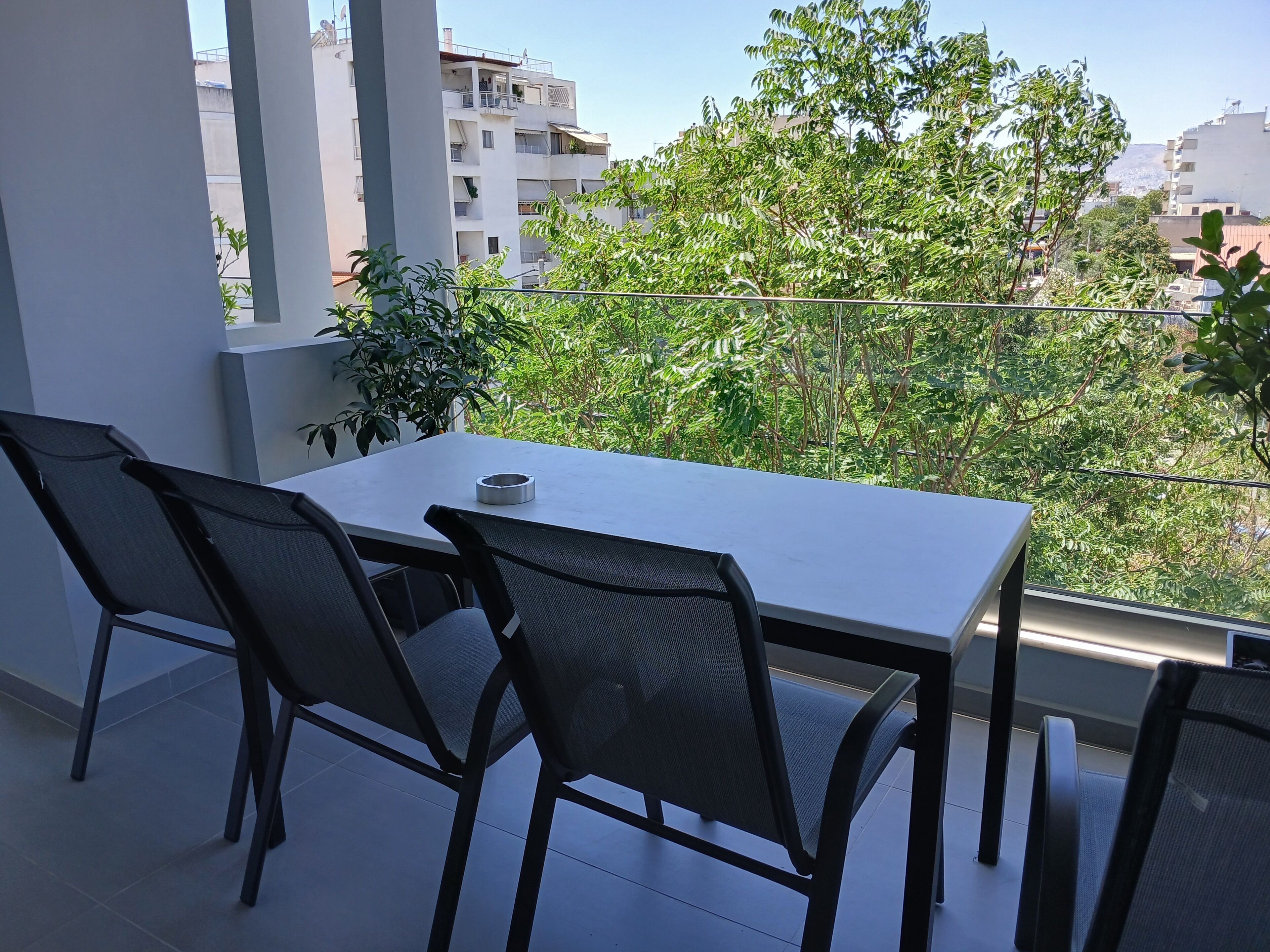 Un balcon avec une table et des chaises, offrant une vue sur le paysage urbain et la verdure.