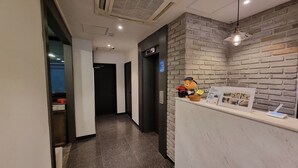 Una recepción con mostrador blanco, pared de ladrillo, un peluche y un cartel con etiqueta de precio.