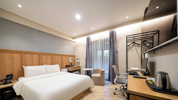 Una habitación de hotel con una cama grande, un escritorio con computadora, una silla, una mesita y un espejo.