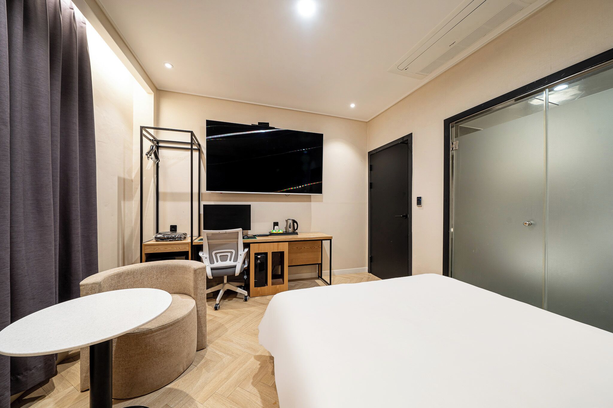 A hotel room with a bed, a desk with a chair, a TV mounted on the wall, and a wardrobe.