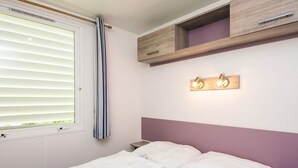 A bedroom with a bed, a window with blinds, a bedside table, and a wall-mounted light fixture. - 4 Person Holiday Park Home in Jelling (Jelling)