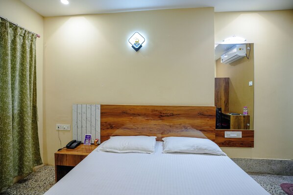 A hotel room with a bed, a nightstand, a phone, a mirror, and a wall-mounted air conditioner. - Chanduka Palace (Puri)