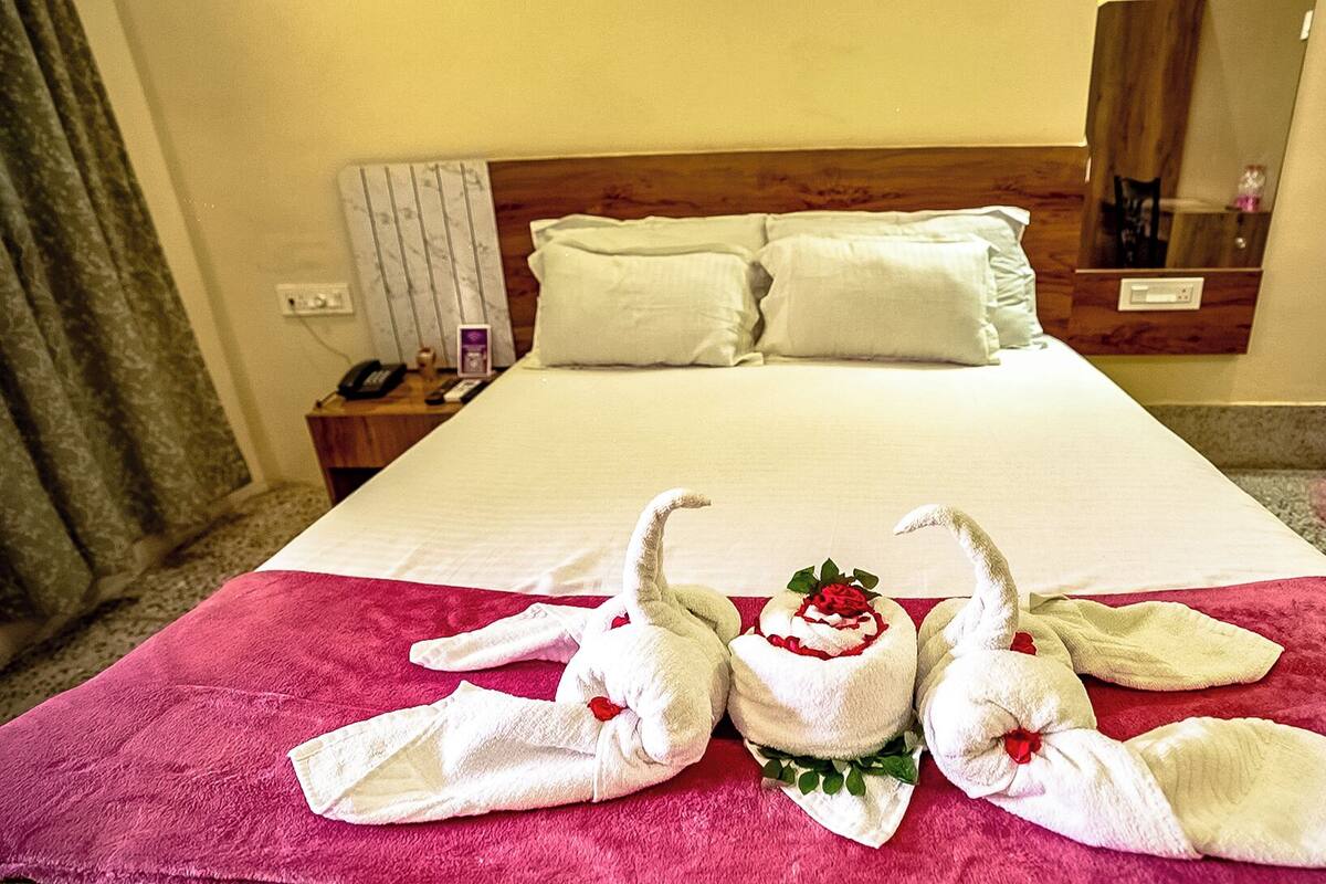 A hotel room with a large bed, two pillows, a nightstand with a phone, and a mirror.