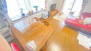 Un accogliente soggiorno con tavolo da pranzo in legno, divano rosso e un divano. Sulla finestra ci sono piante in vaso e un calendario appeso al muro.