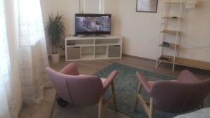 A living room with a television on a white stand, two pink chairs, a potted plant, and a framed picture on the wall. - Unique apartment in the Hundertwasserhaus in the center of Plochingen

 (Plochingen)
