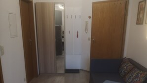 A compact living space with a kitchenette, a sofa with a colorful cushion, and a wooden wardrobe. - Unique apartment in the Hundertwasserhaus in the center of Plochingen

 (Plochingen)