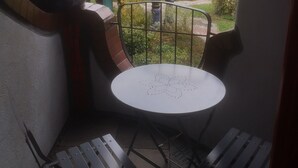 A small balcony with a round table and two chairs, overlooking a garden and buildings with unique architecture. - Unique apartment in the Hundertwasserhaus in the center of Plochingen

 (Plochingen)