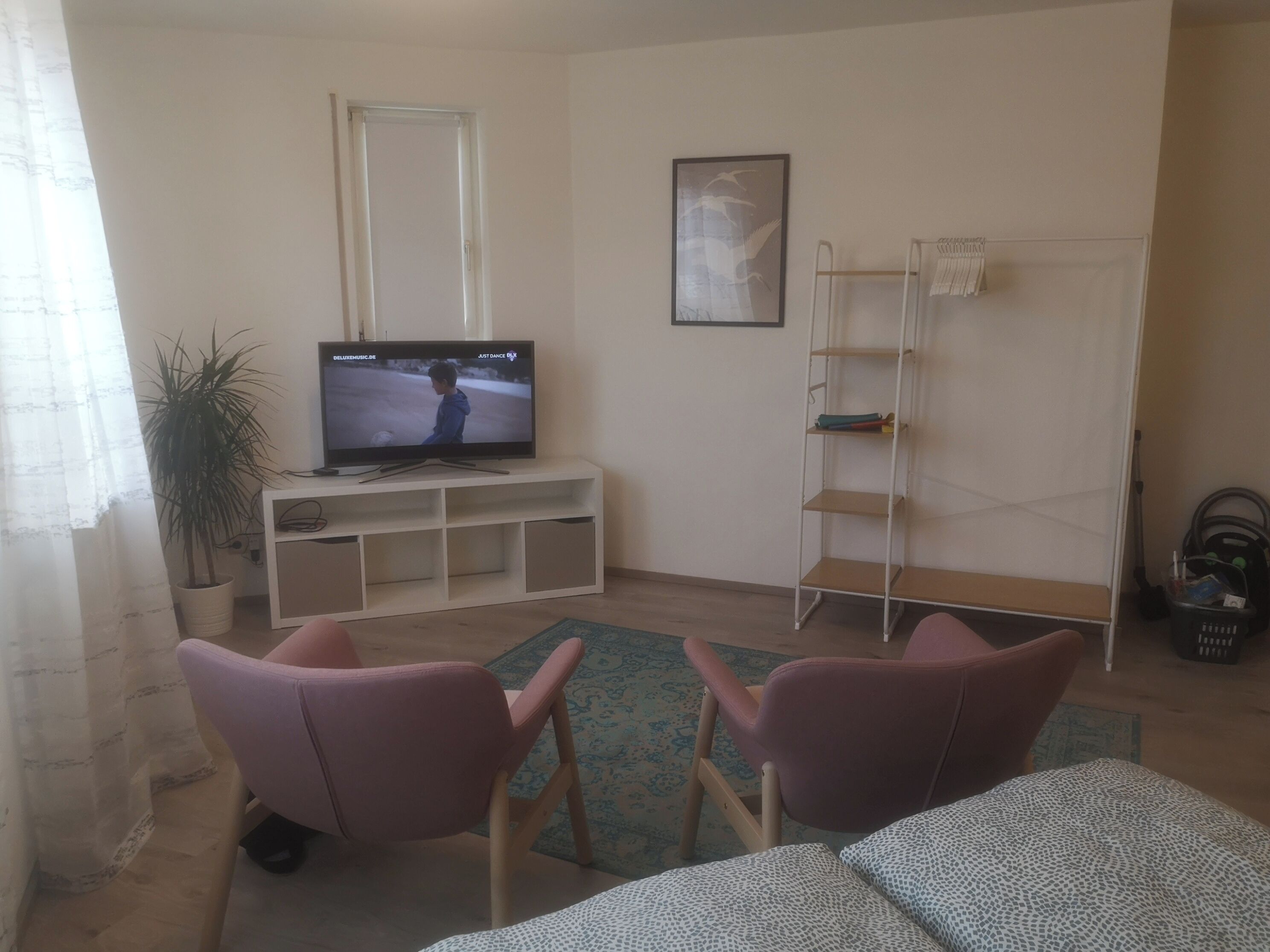 Una sala de estar con televisor, dos sillas, un sofá, una planta en maceta, un estante y una escalera.